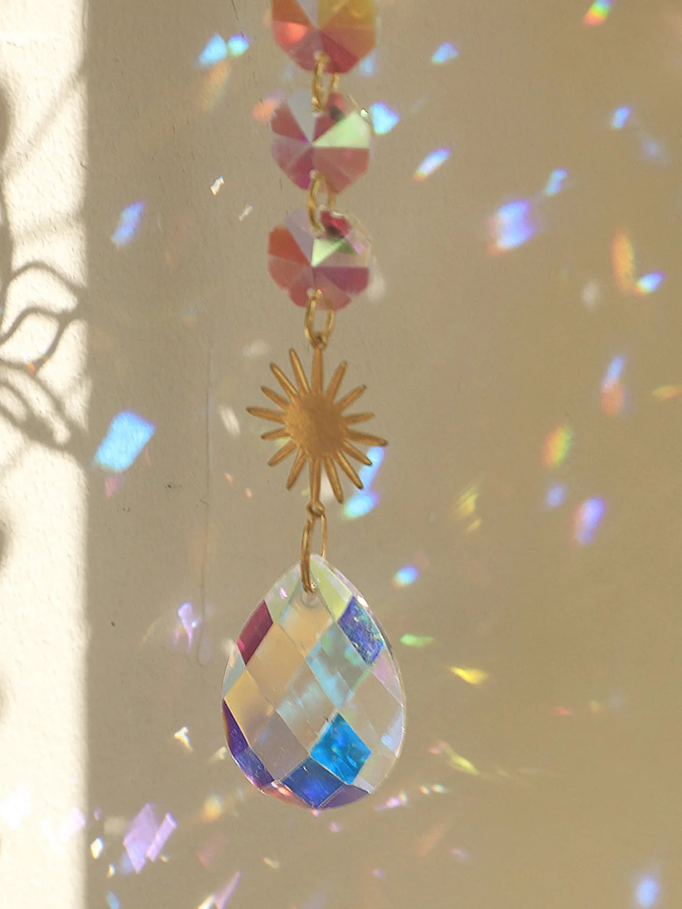 Colorful hanging crystal with a gold sun-shaped charm against a neutral background