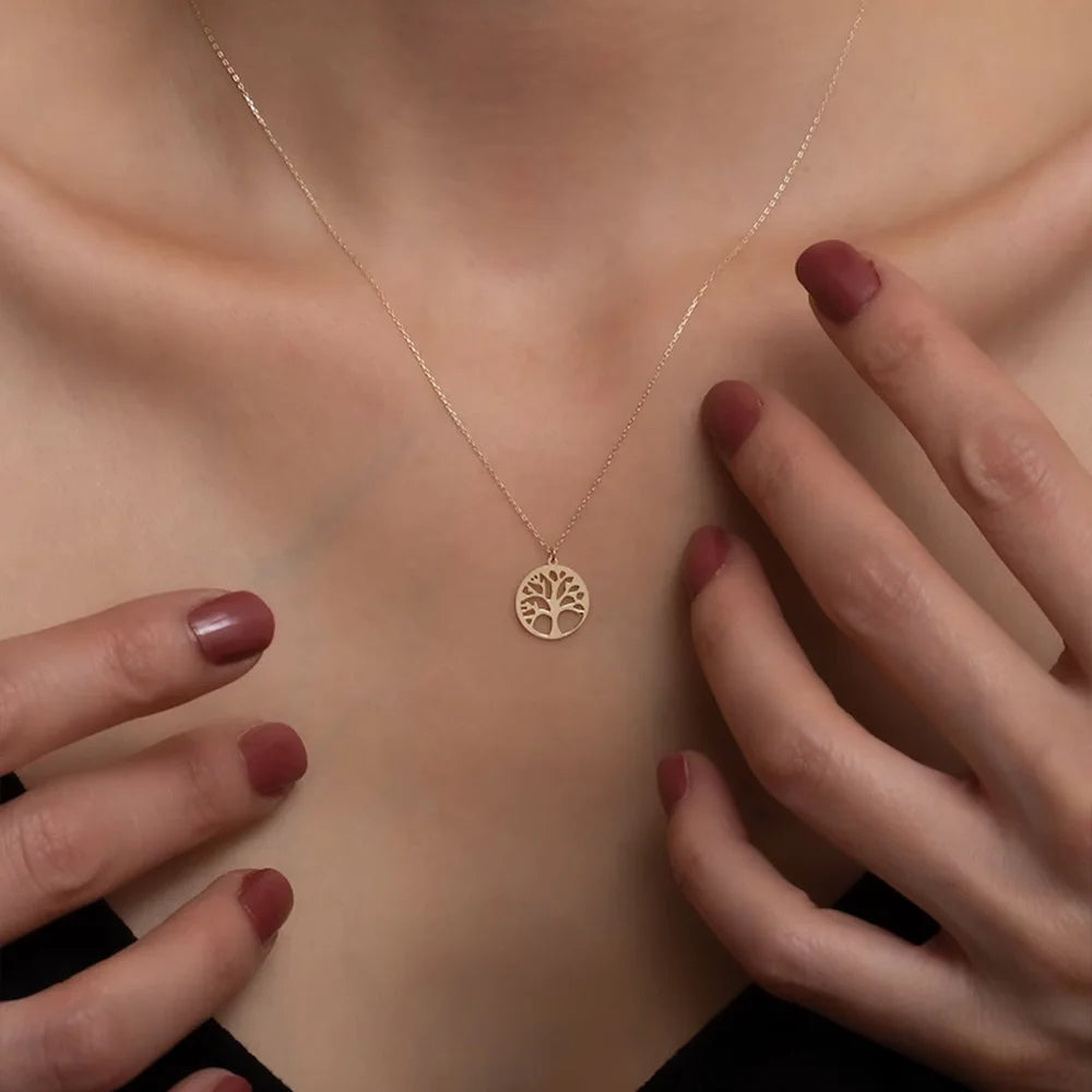 Gold necklace with a tree-of-life pendant on a person's neck, with hands gently touching the skin.