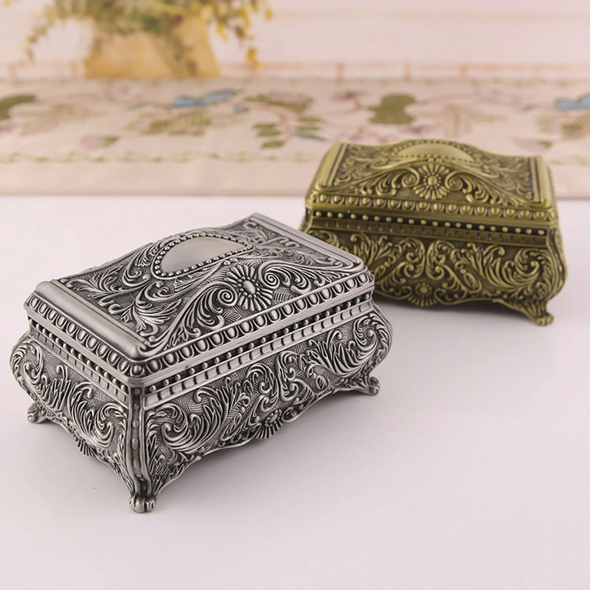 Two ornate jewelry boxes, one silver and one bronze, on a light background.