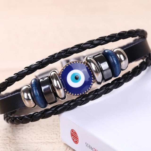 Black braided leather bracelet with blue evil eye charm on a beige background
