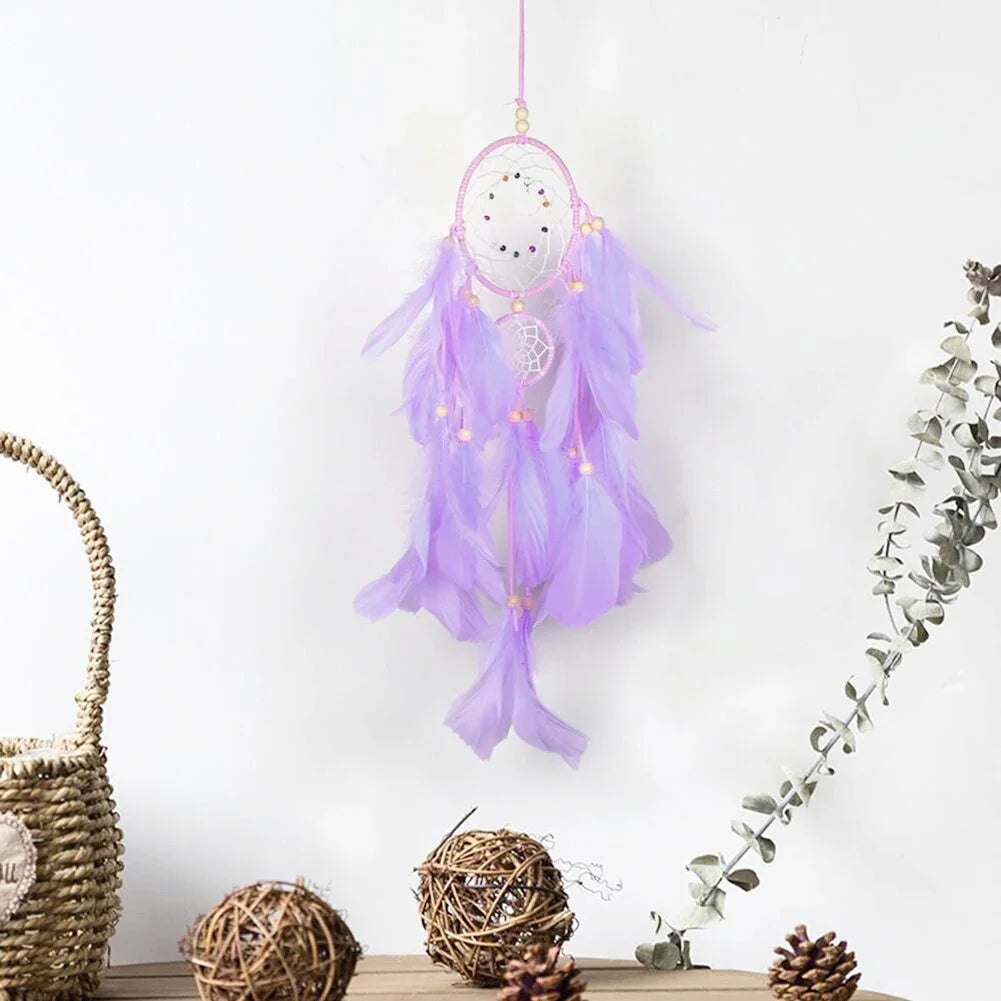 Purple dreamcatcher with feathers and lights hanging on a white wall with decorative elements below.