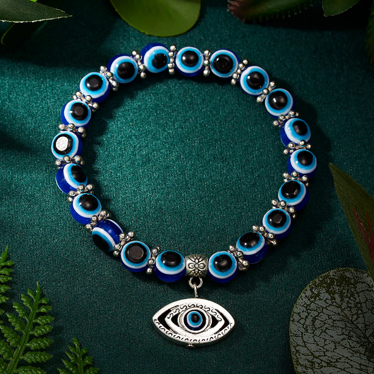 Blue and black beaded bracelet with an eye charm on a green fabric background