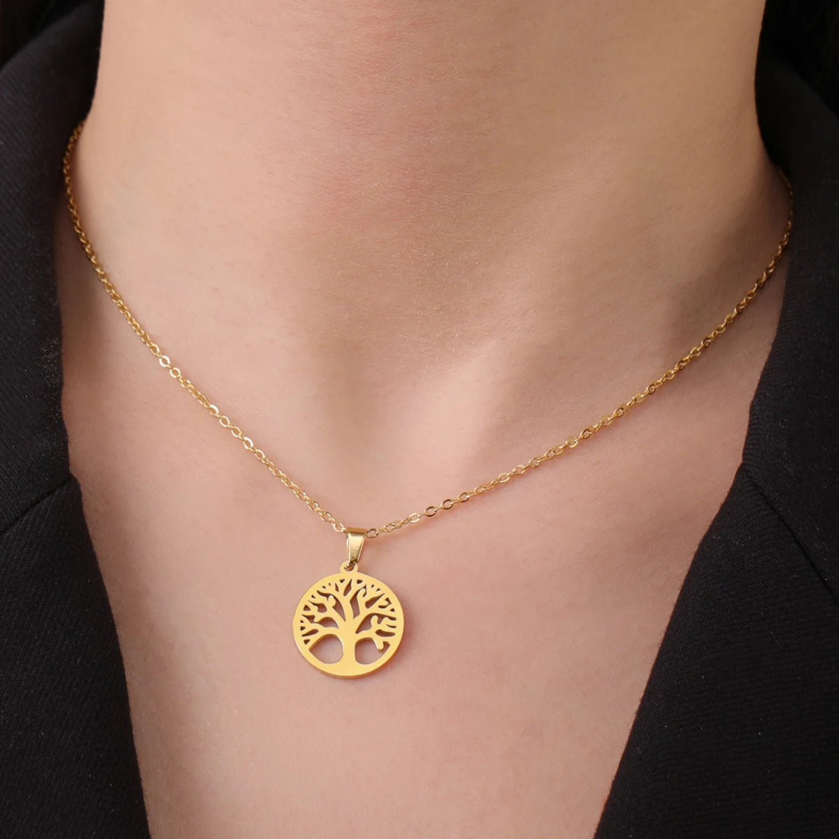 Gold necklace with a tree pendant on a person wearing a black outfit.