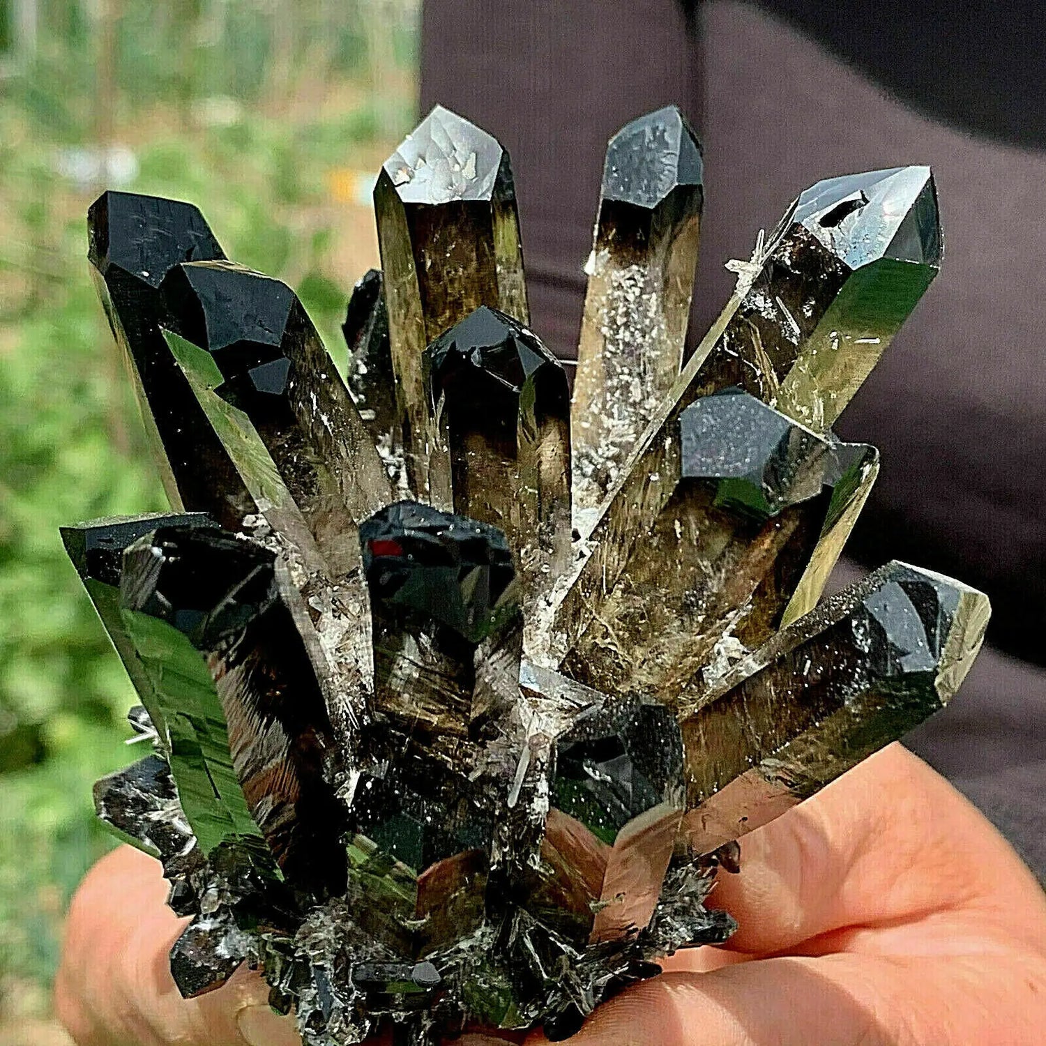 Hand holding a cluster of crystal formations with a blurred natural background
