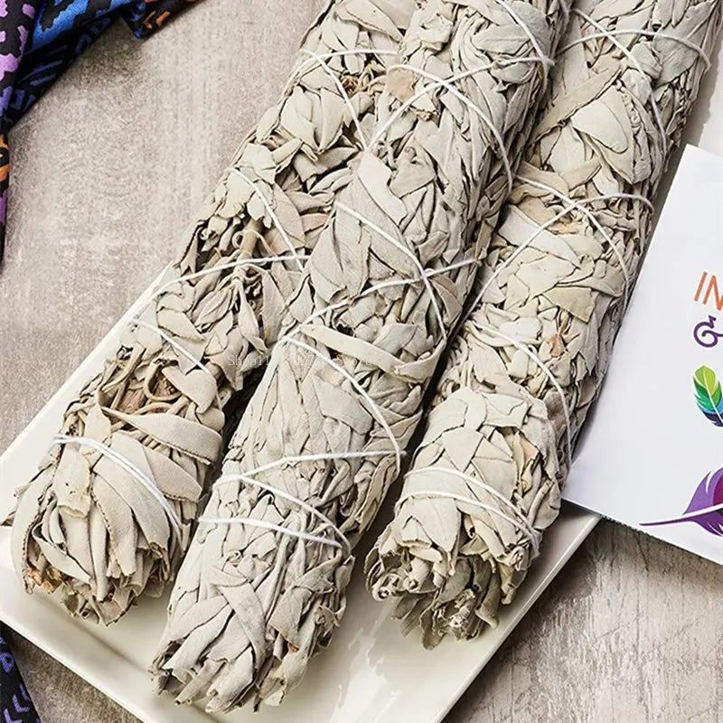 Three bundles of sage wrapped in twine on a white plate with a colorful card in the background.