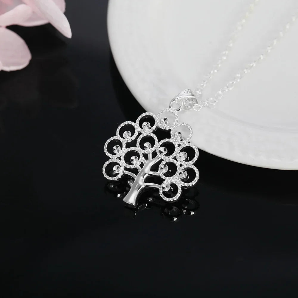 Silver tree-shaped pendant on a dark surface with a white plate in the background