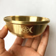 Gold bowl with engraved symbols held by a hand against a white background