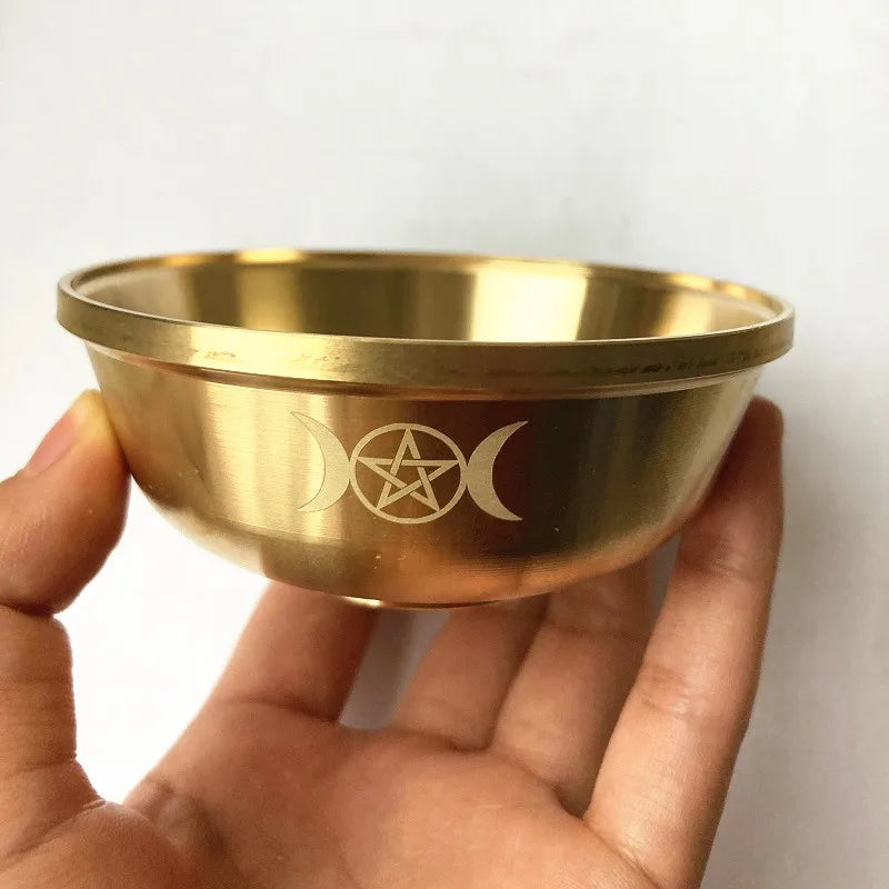 Gold bowl with engraved symbols held by a hand against a white background