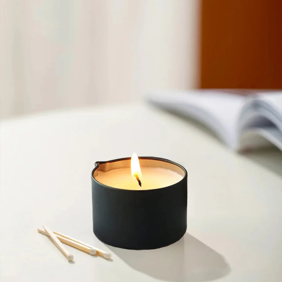 Lit candle in a black container on a white surface with matches beside it.