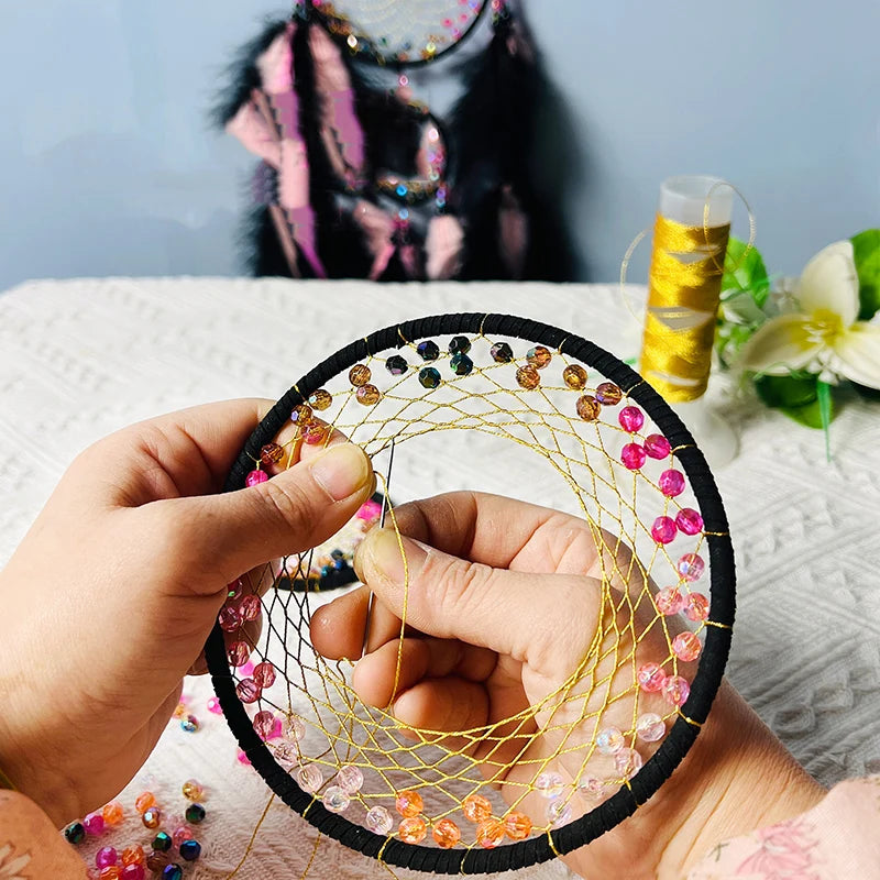 Hand holding a beaded dreamcatcher with beads being added, blurred background