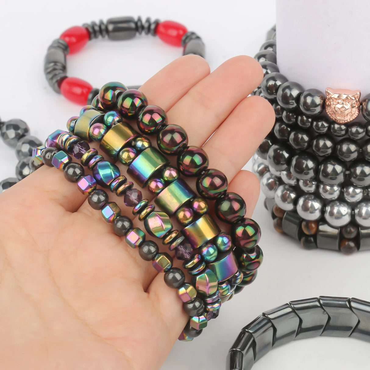 Hand holding colorful beaded bracelets with additional bracelets in the background on a white surface.