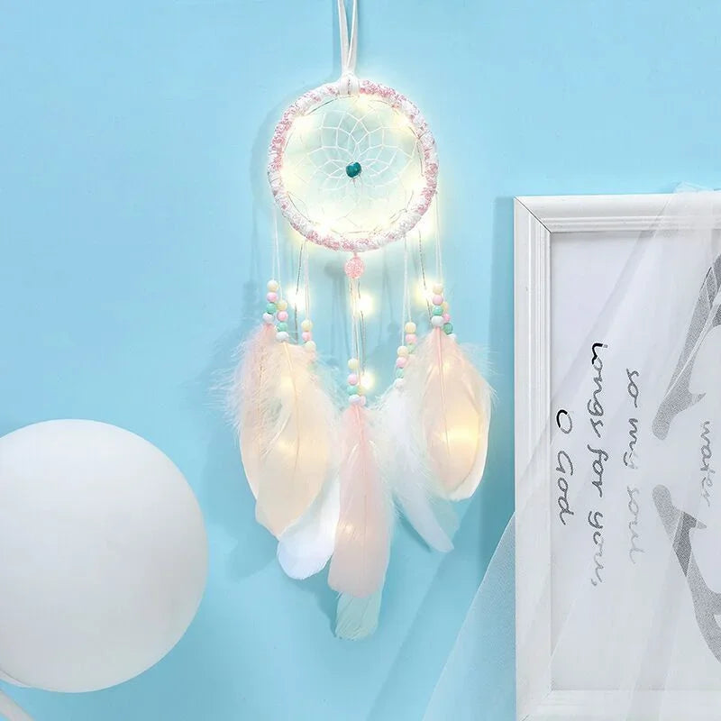 Decorative dreamcatcher with feathers and lights on a light blue wall.