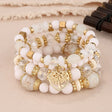 Stack of white and gold beaded bracelets with a heart charm on a beige fabric background