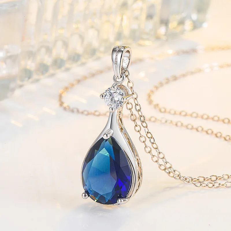 Jewelry pendant with blue teardrop stone and clear gem on a blurred background