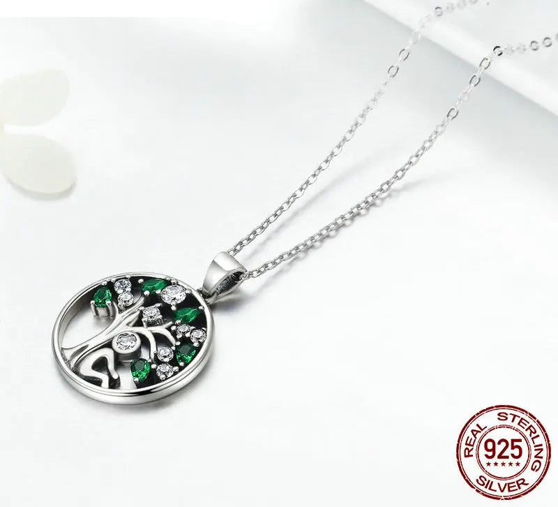 Silver necklace with a tree of life pendant featuring green and clear stones on a white background, branded WOSTU.