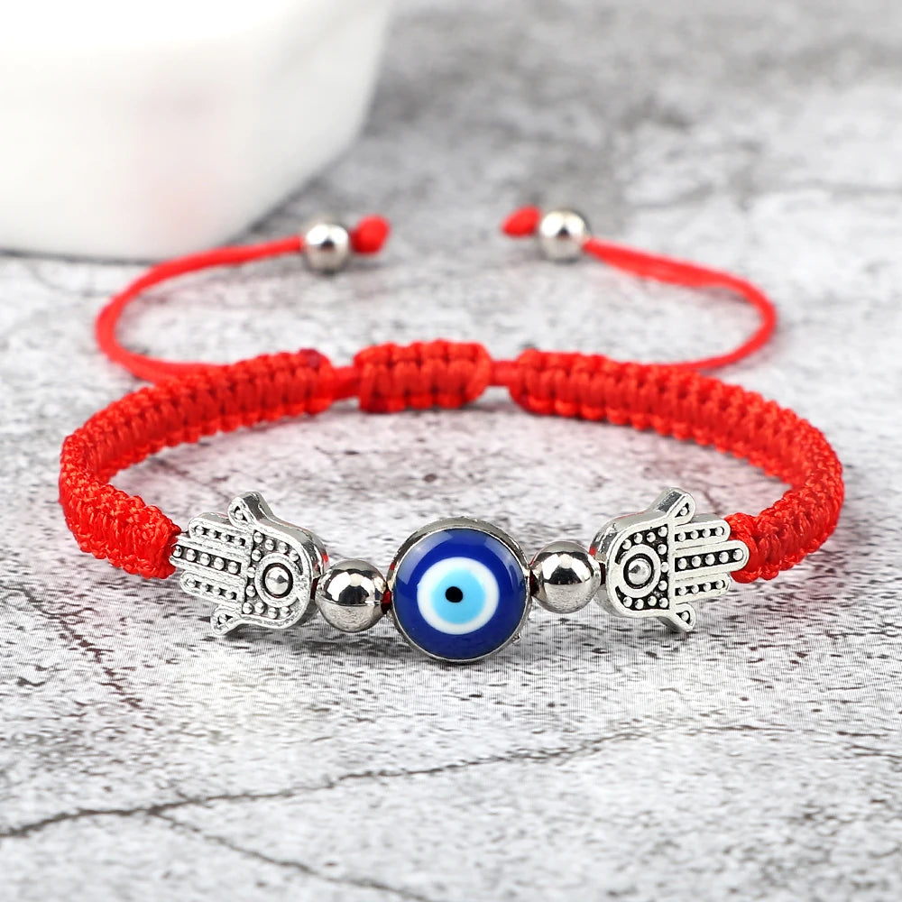 Red bracelet with Hamsa hand and evil eye charm on a textured surface