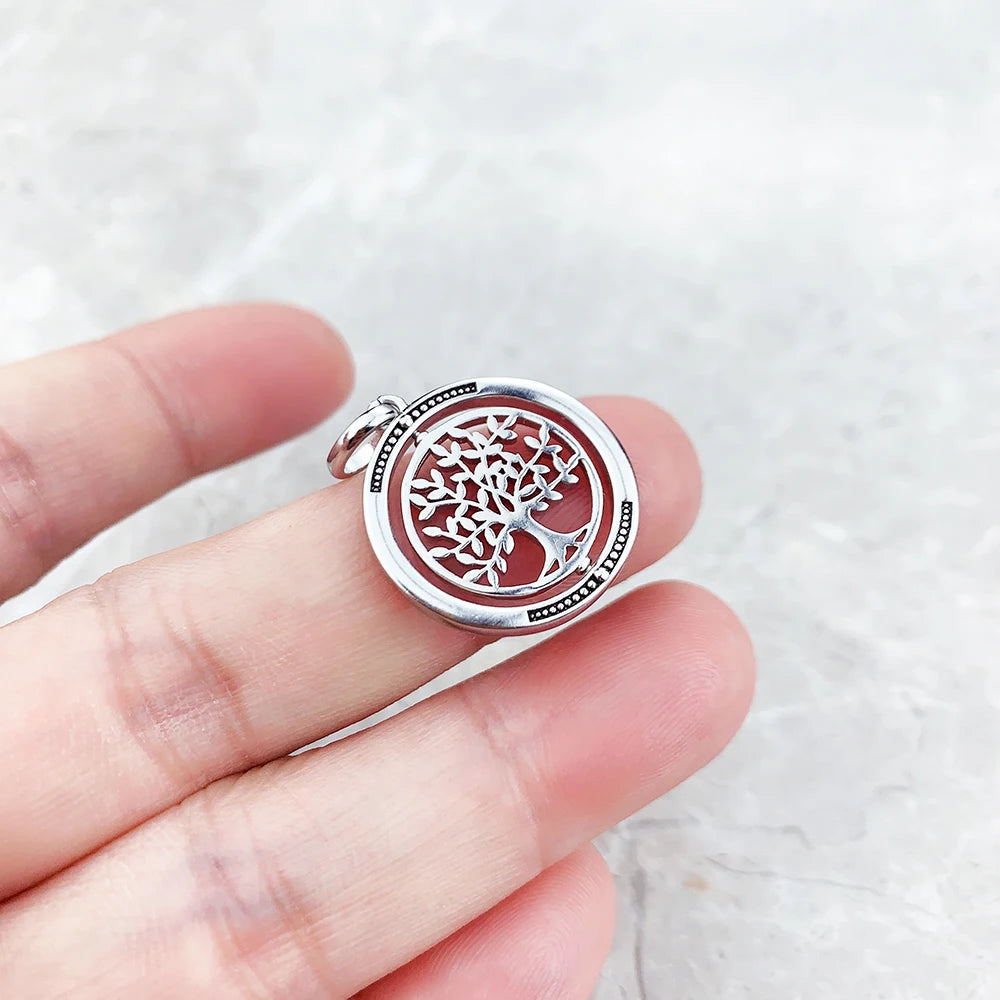 Silver pendant with tree of life design held in a hand against a light background