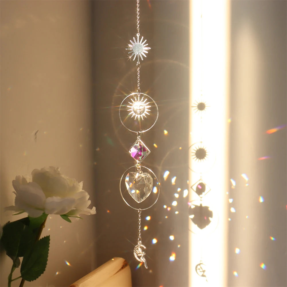 Decorative hanging crystal with sun, moon, and star designs in front of a window with a rose.