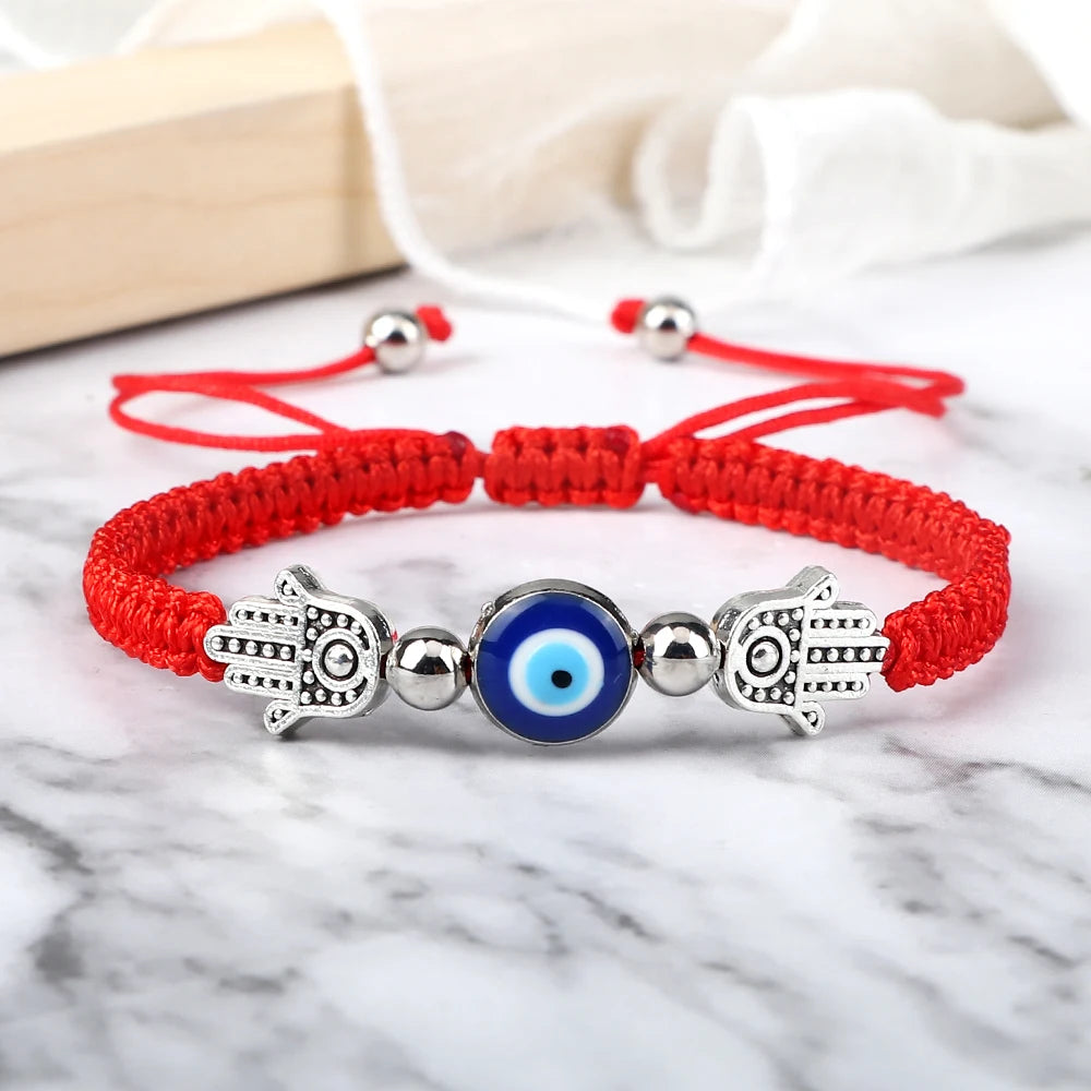 Red bracelet with silver Hamsa hand and blue evil eye bead on a marble surface