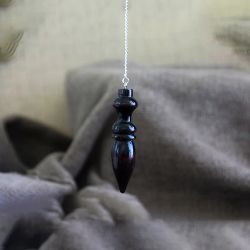 Black decorative object hanging on a chain against a neutral background