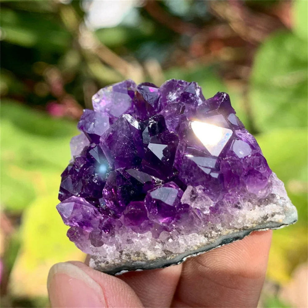 Amethyst crystal cluster held in a hand with a blurred green background