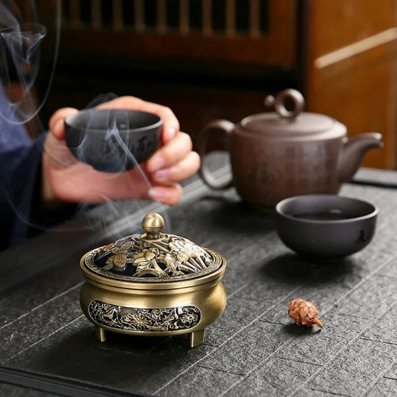 Tea ceremony setup with a person holding a cup, teapot, and incense burner on a dark surface.