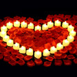 Heart shape made of red rose petals and white candles on a black background