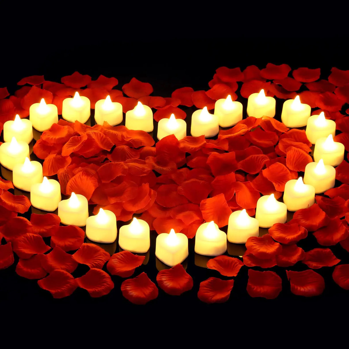 Heart shape made of red rose petals and white candles on a black background