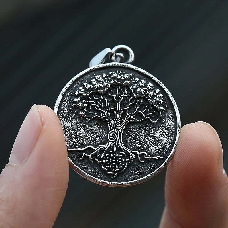 Silver tree pendant held between fingers against a dark background