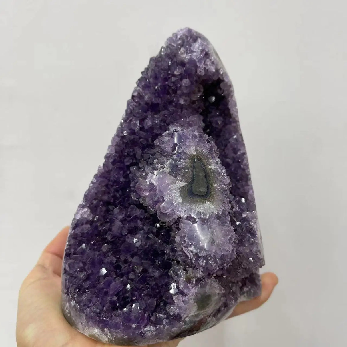 Amethyst crystal with a hand holding it against a plain background