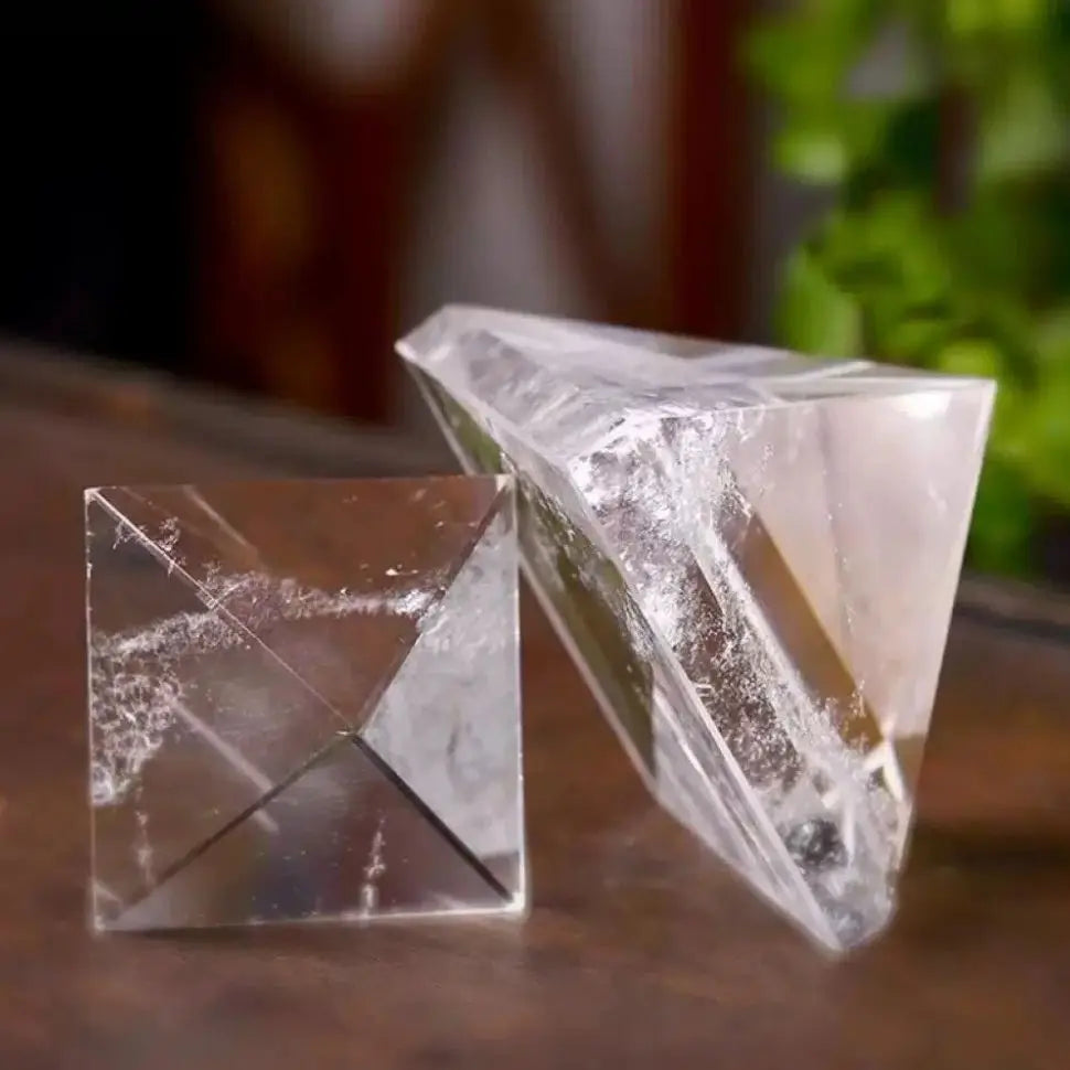 Two crystal prisms on a wooden surface with a blurred natural background