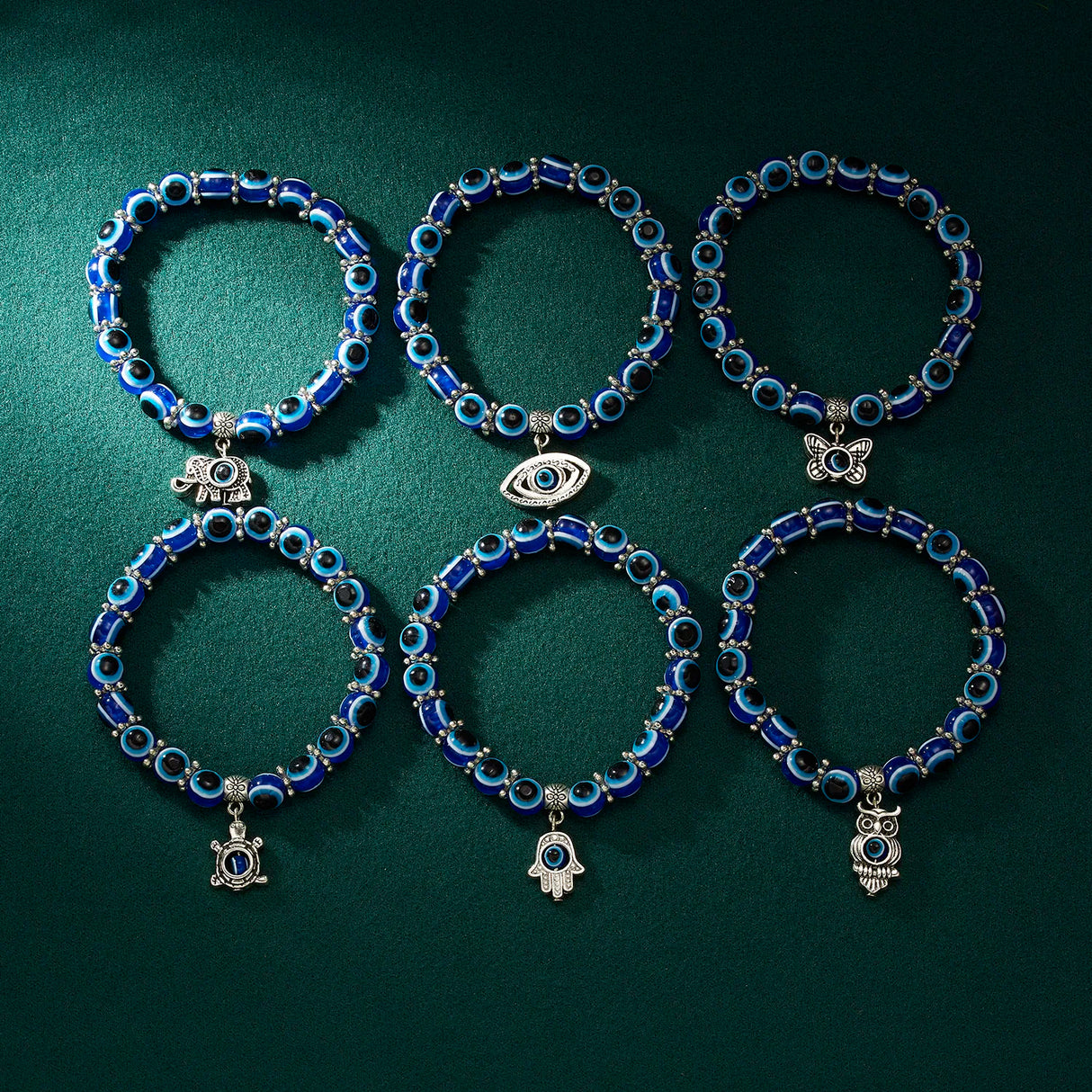 Set of five blue beaded bracelets with various charms on a dark green background