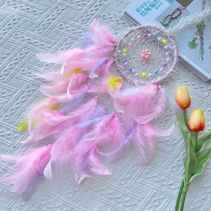 Pink feathered dreamcatcher with colorful beads on a textured surface with tulips.