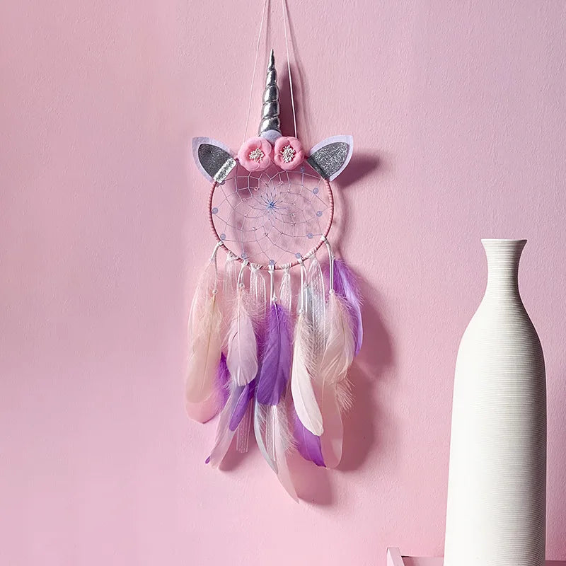 Unicorn-themed dreamcatcher with feathers on a pink wall next to a white vase.