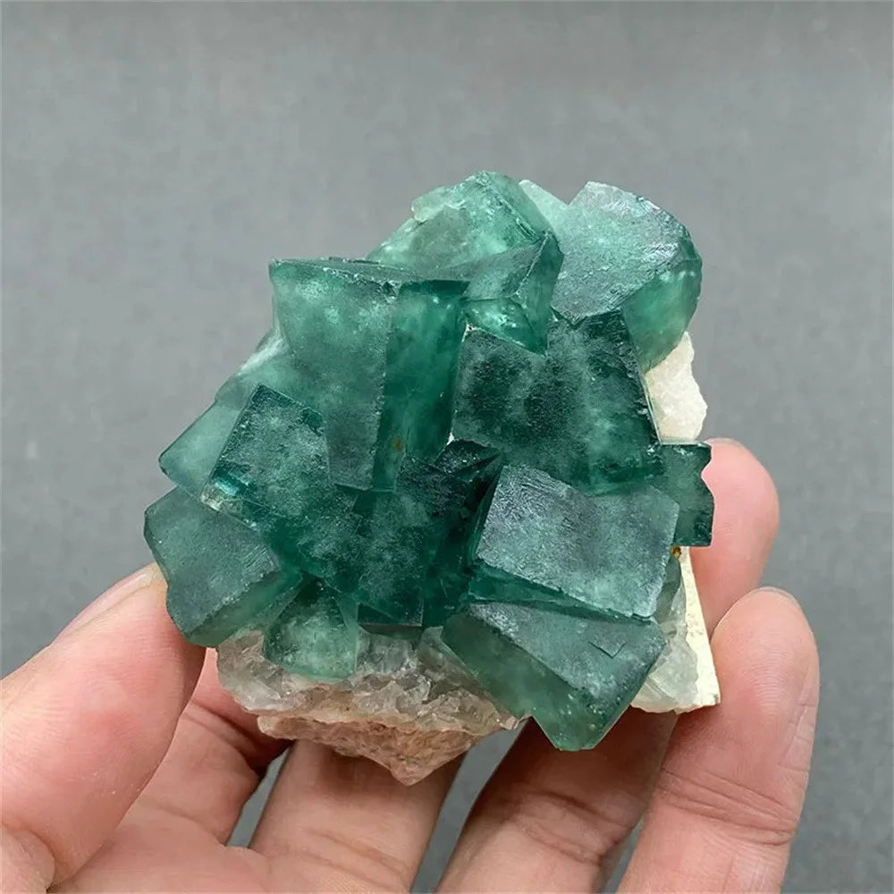 Green crystal cluster held in a hand against a gray background