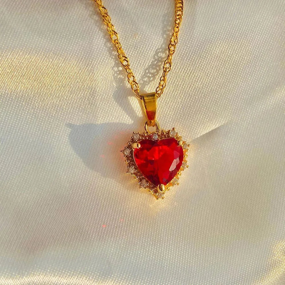 Gold necklace with a red heart-shaped pendant on a light fabric background