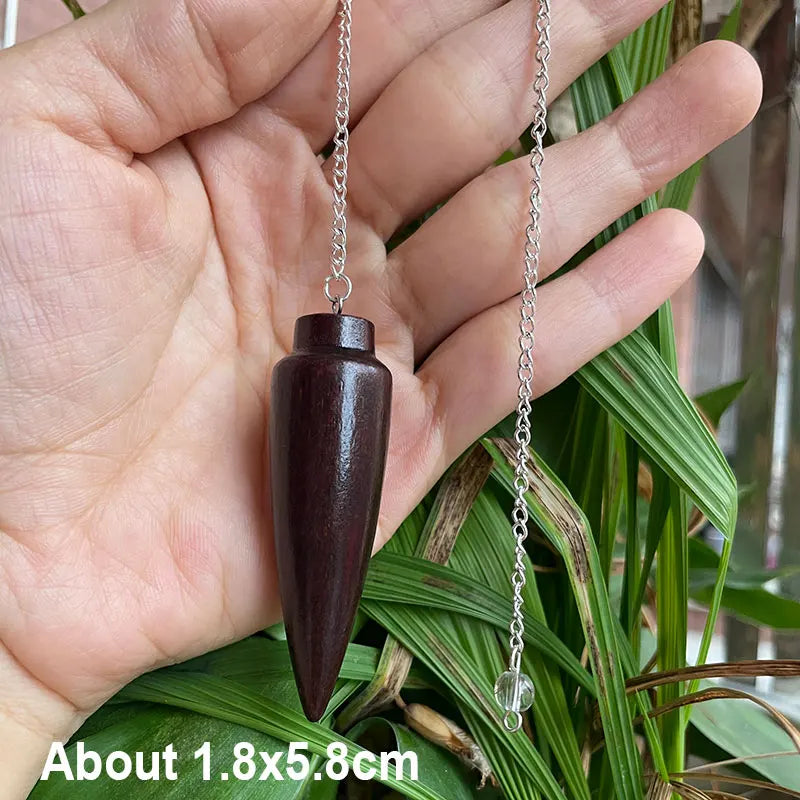 Wooden pendulum on a chain held in a hand with green leaves in the background