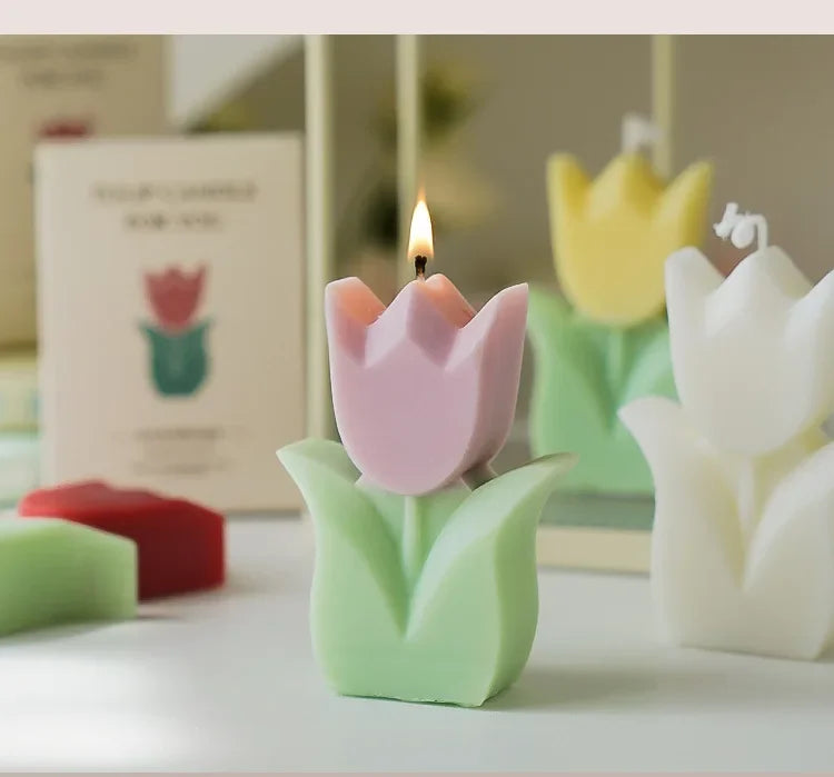 Pink tulip-shaped candle with a green base on a white surface, with a blurred background.