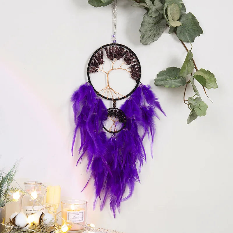 Dreamcatcher with purple feathers hanging against a white wall with greenery.