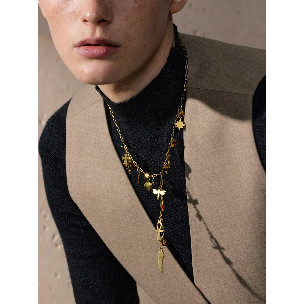 Person wearing a gold necklace with various pendants against a neutral background