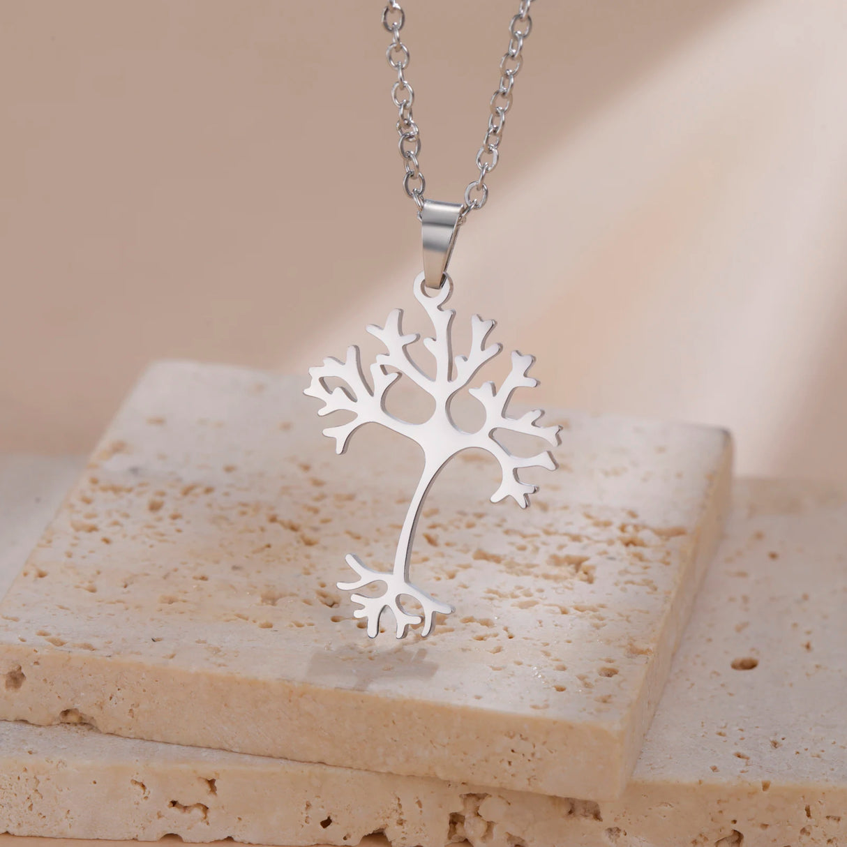 Silver tree-shaped pendant on a beige stone surface