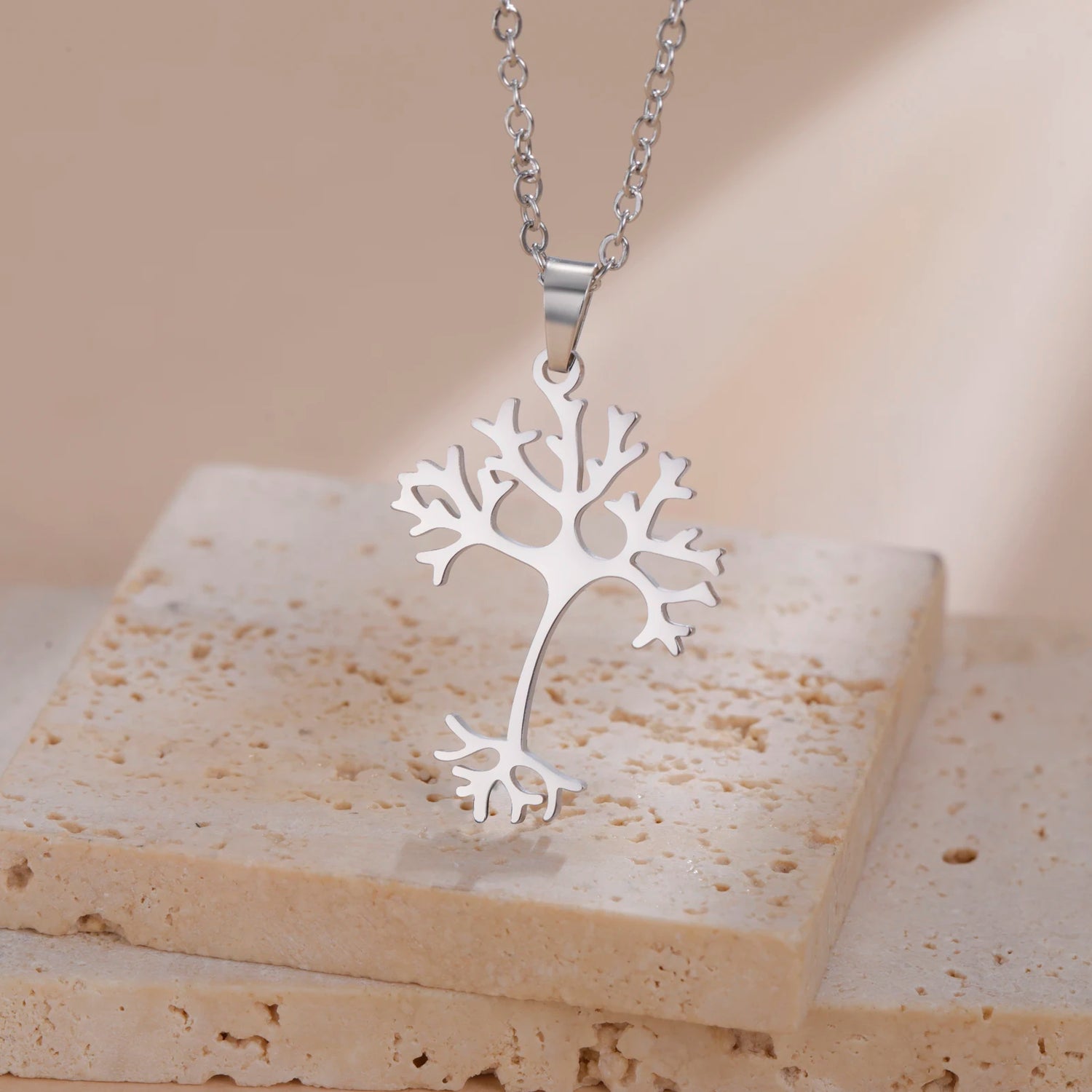 Silver tree-shaped pendant on a beige stone surface