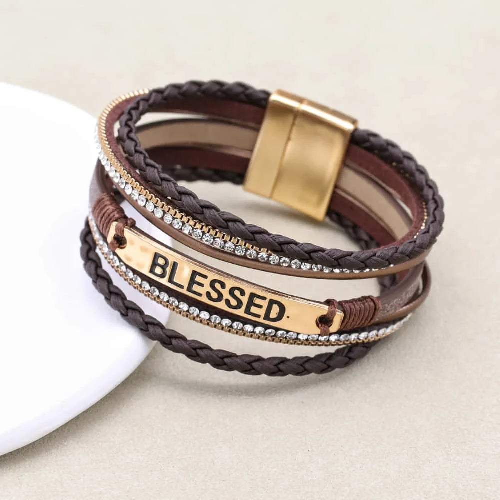 Multistrand leather bracelet with gold accents and 'BLESSED' tag on a beige background