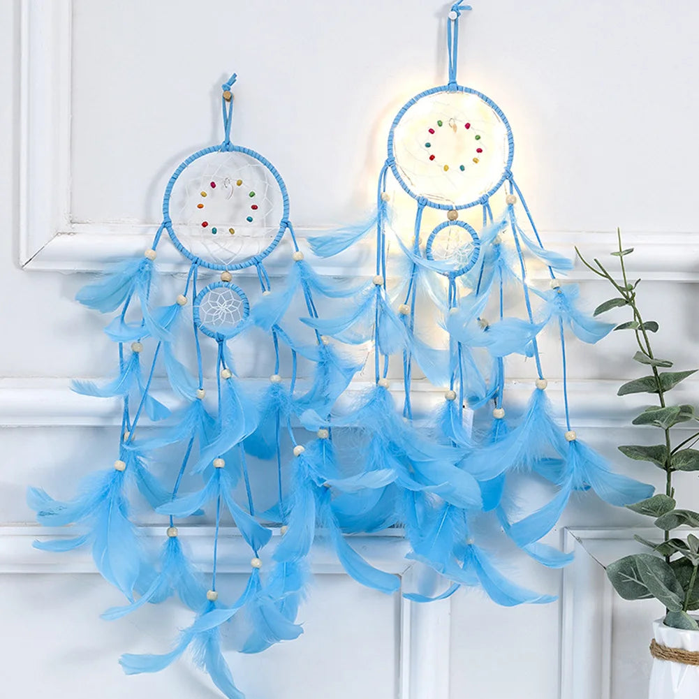 Blue dreamcatcher hanging on a white wall with a plant in the corner.