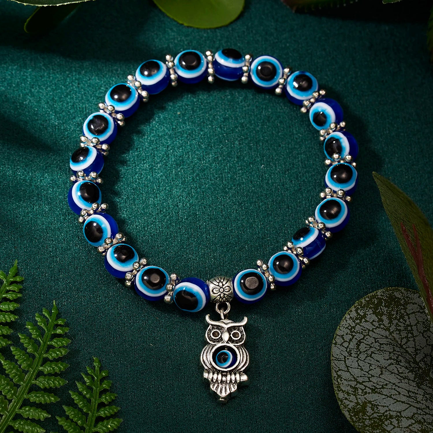 Bracelet with blue and black beads and an owl charm on a green leafy background