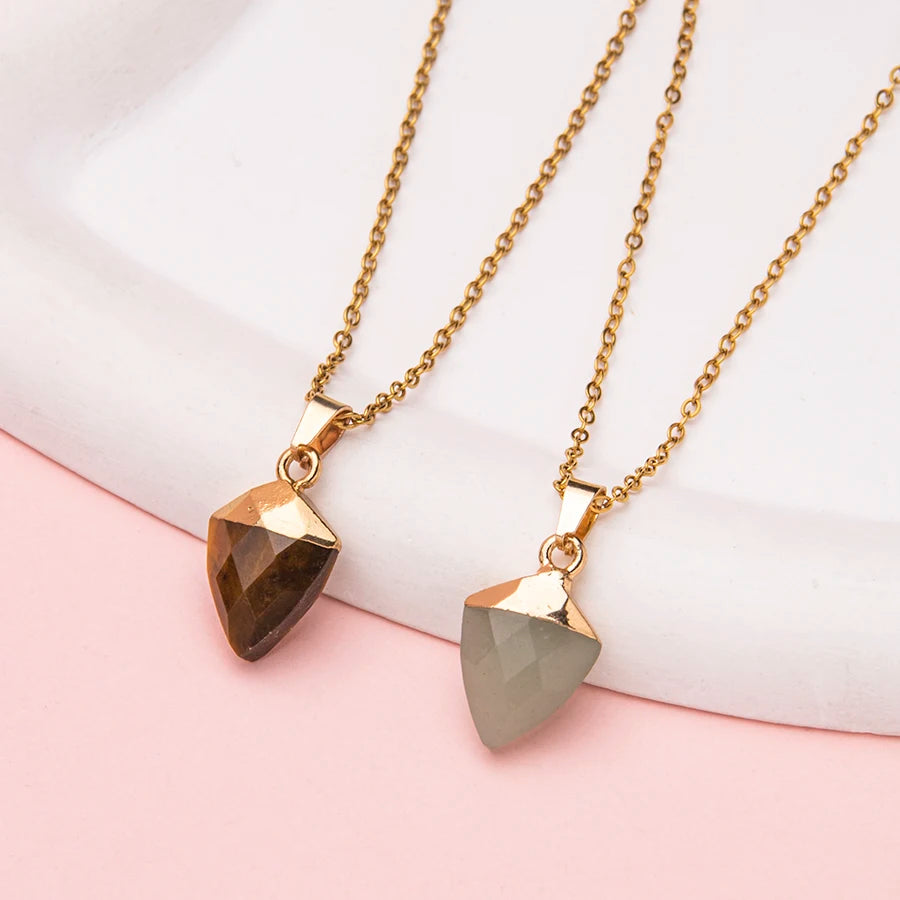 Two gold necklaces with teardrop-shaped pendants on a light pink background