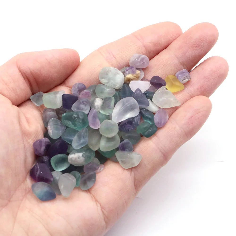 Hand holding a small pile of multicolored gemstones against a white background