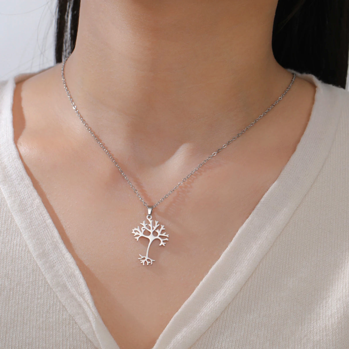 Silver tree-shaped pendant necklace on a person wearing a white shirt.