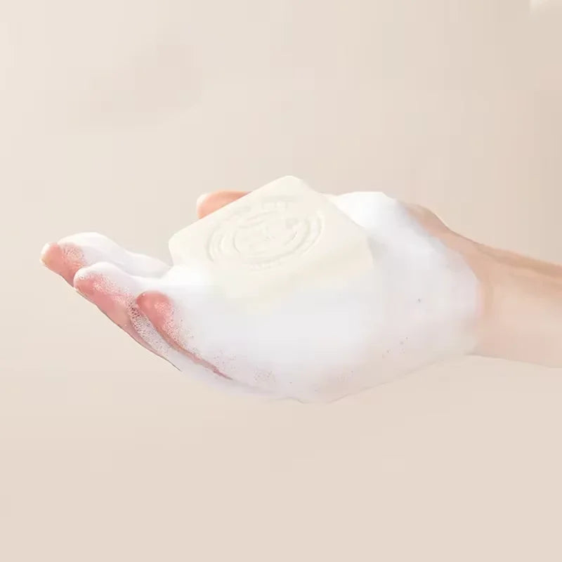 Hand holding a bar of white soap with a light beige background