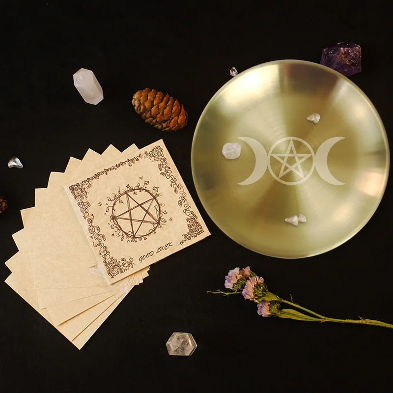 Witchcraft items including a gold trident plate, cards with pentacle symbols, crystals, and flowers on a dark background.